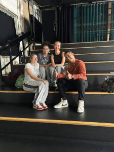 Acea assise avec trois élèves sur les gradins du studio, tous souriants.